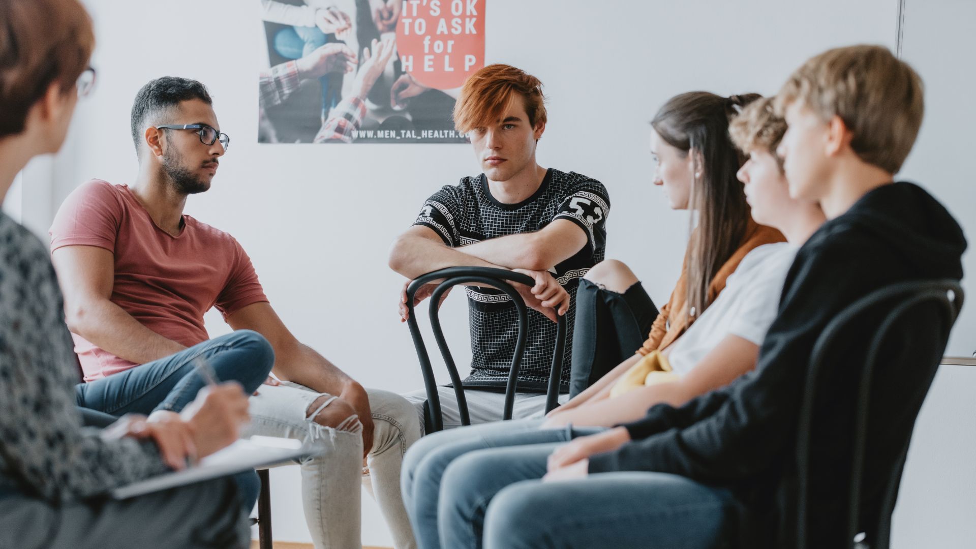 A group of teenagers sit in a circle during a group therapy session.