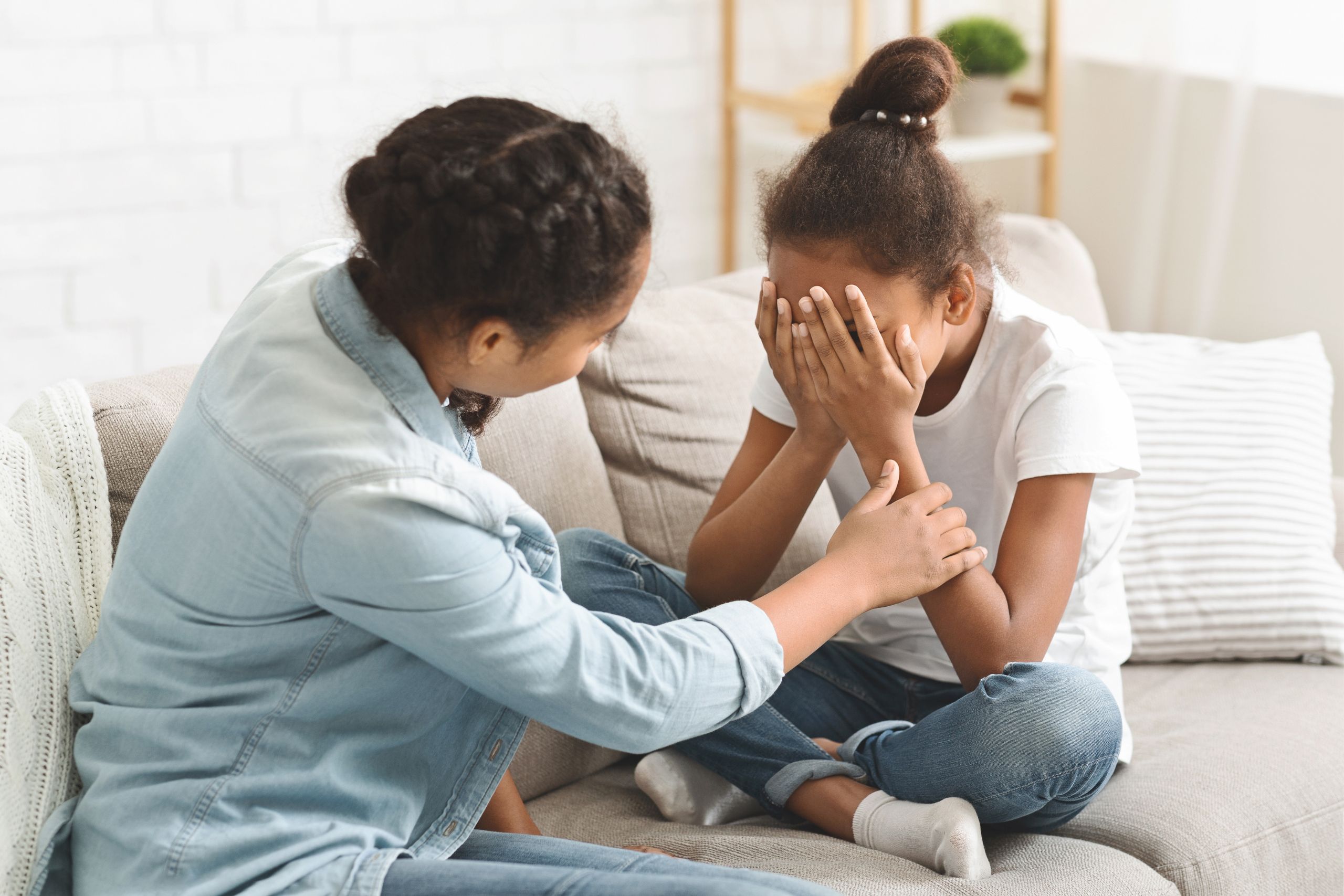 A mother tries to comfort her crying daughter on the couch.