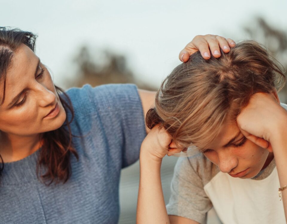 A mother rubs the top of her son's head as he looks down, sadly.