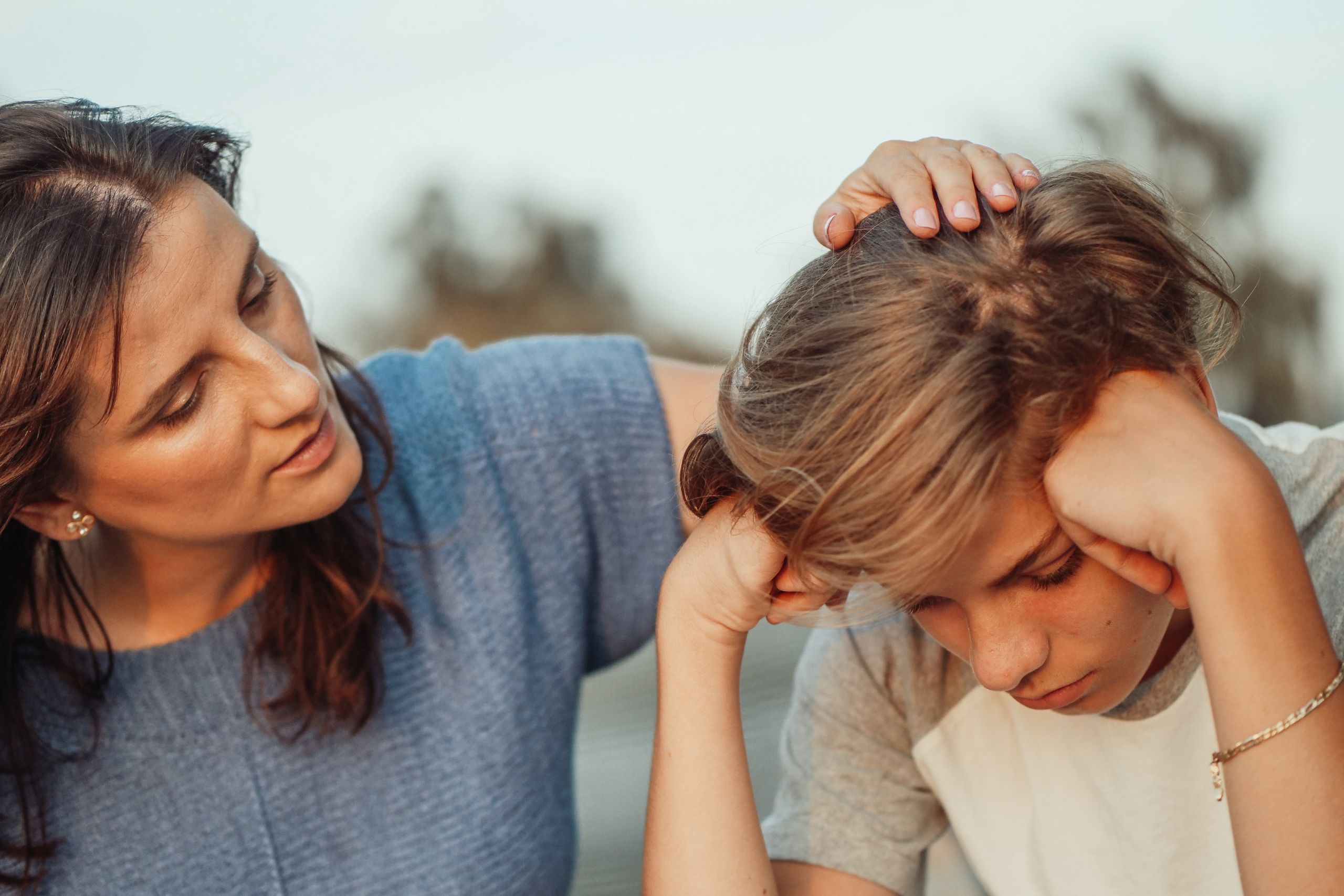 A mother rubs the top of her son's head as he looks down, sadly.