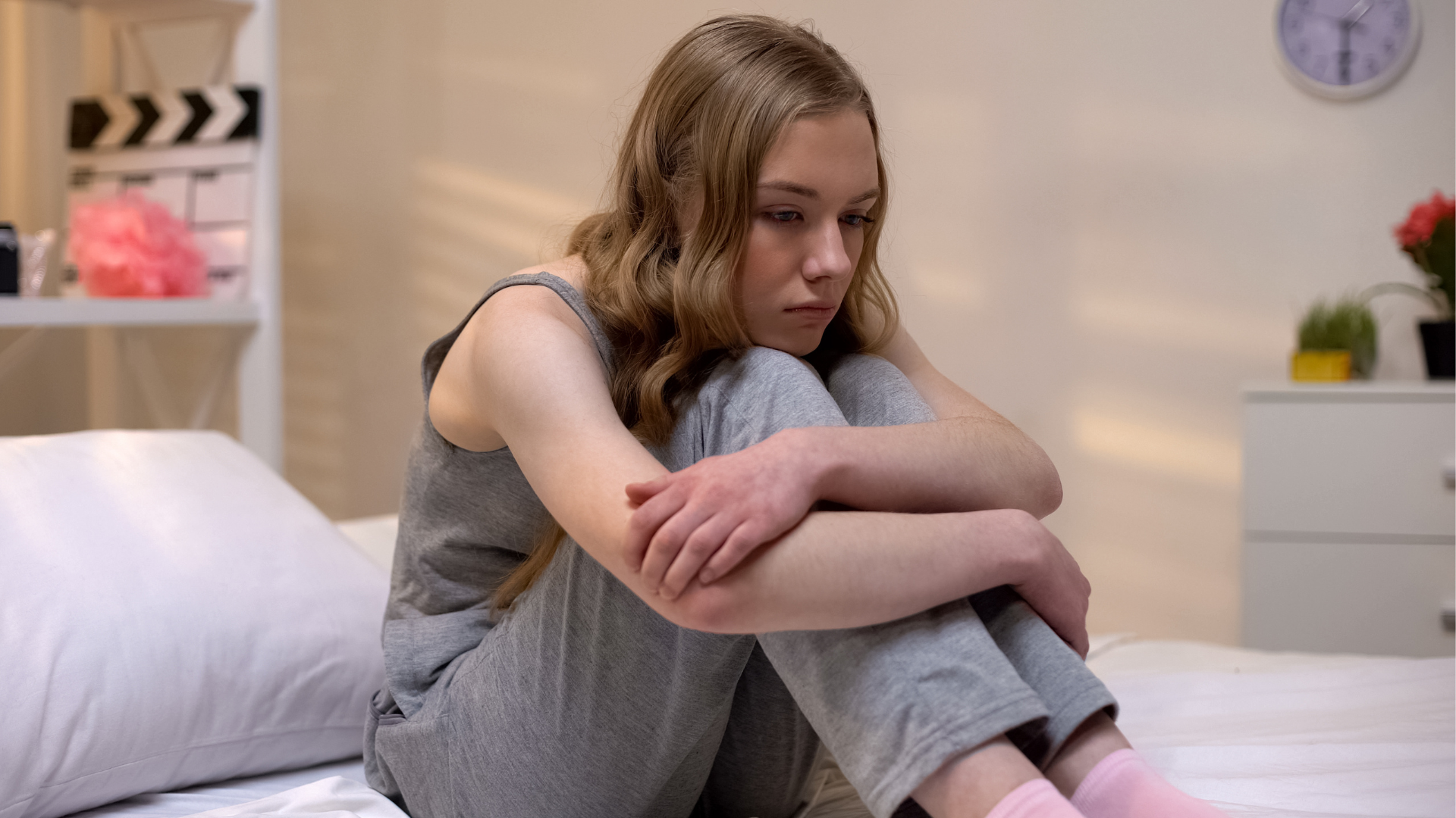 teen girl on a bed with her chin resting on her knees and her arms crossed over her shins.