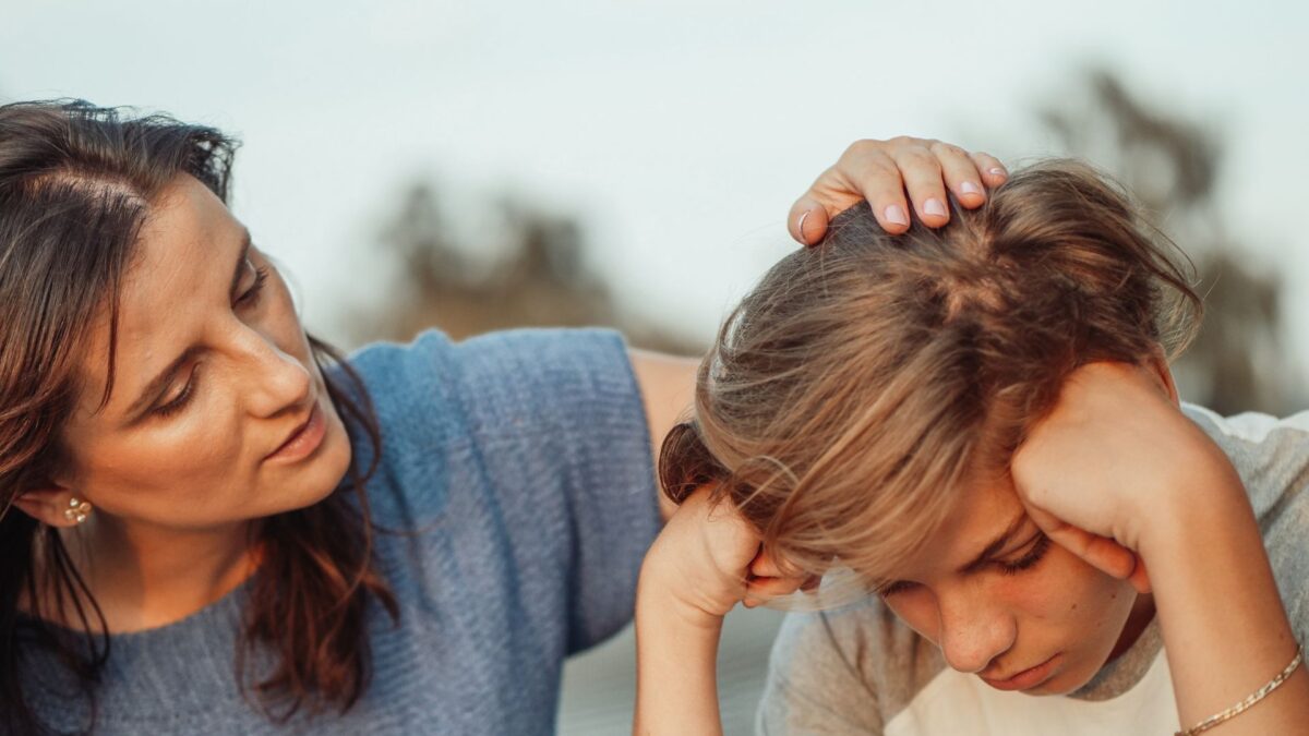 A mother pats the head of her son who is looking sad.