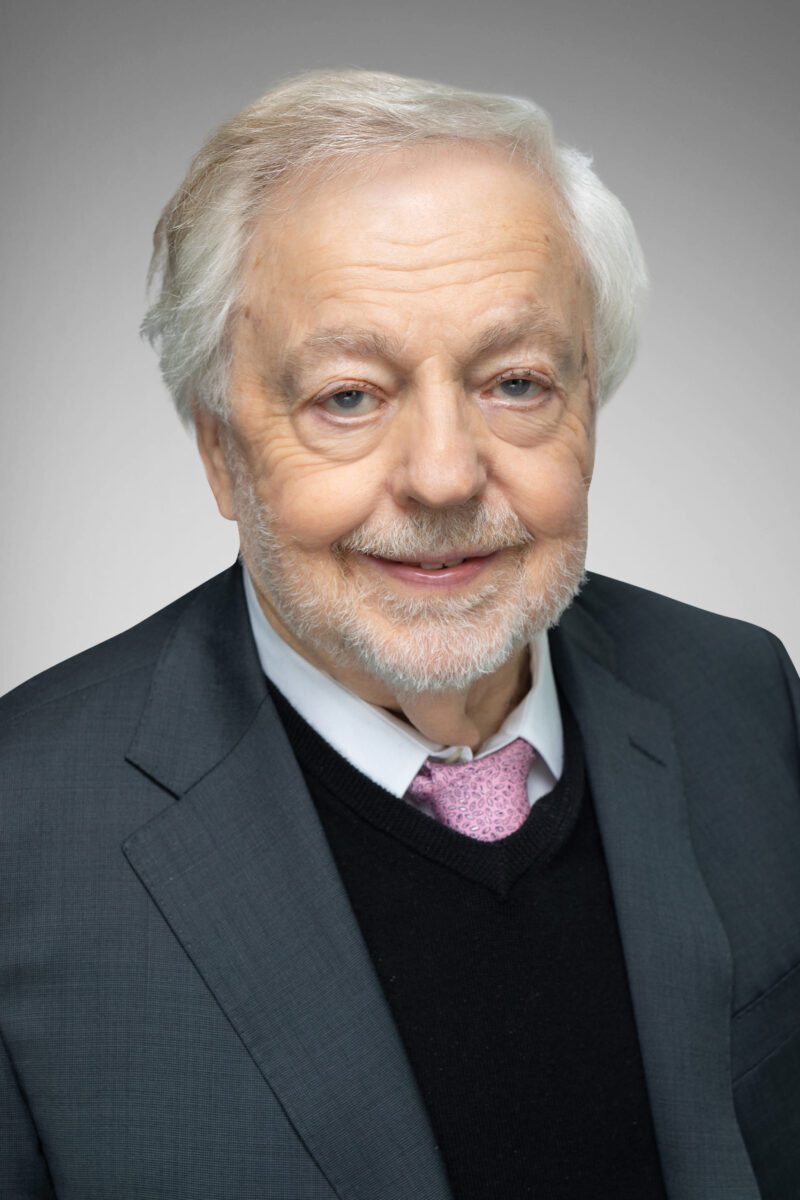 Man in a dark gray suit smiling with gray hair.