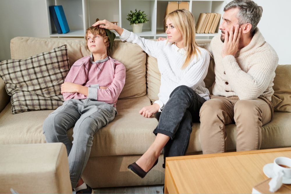 A mother and father consider therapy for their teenage son as they sit on the couch near him.