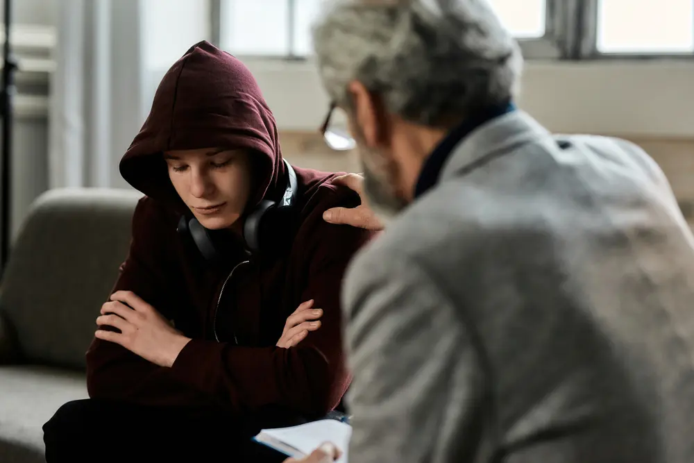 Adult man talking to a teen wearing a hoodie and headphones.