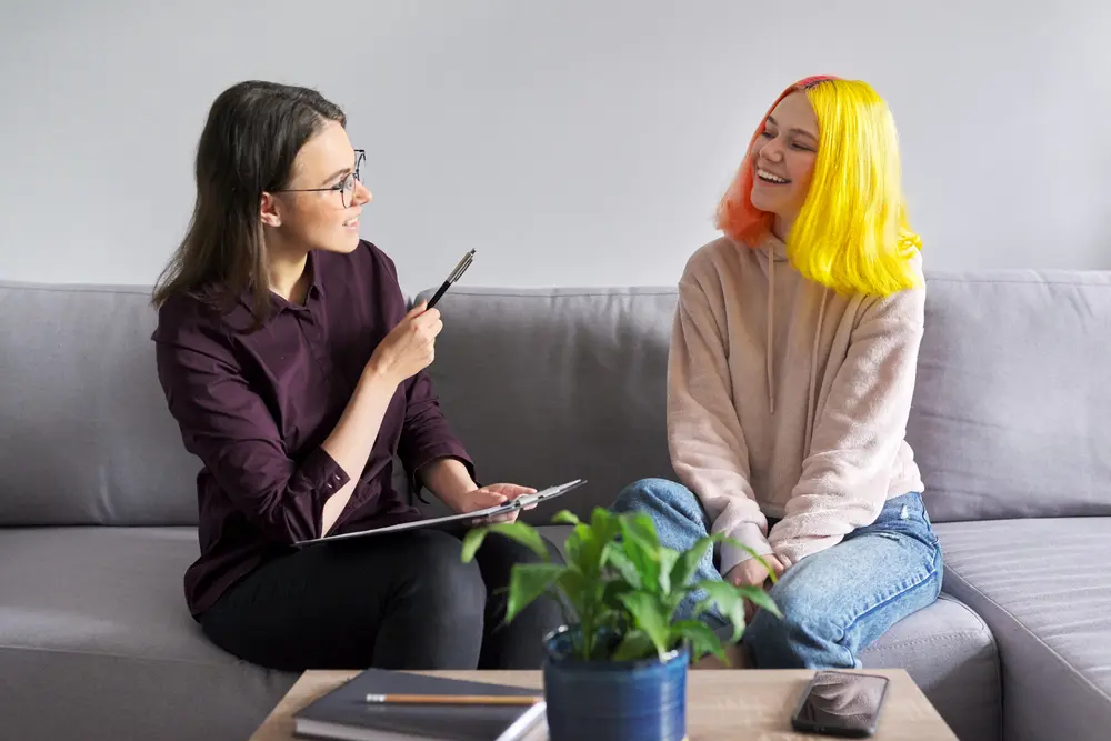 Therapist and teen sit together and talk and smile.