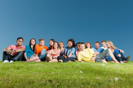 A group of teenagers sit on a grassy hill.