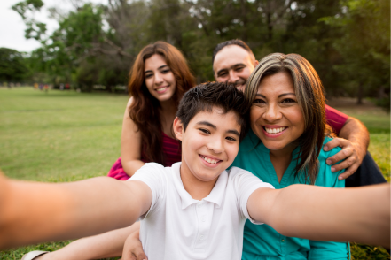 A teenage boy smiles at the camera for a selfie with his parents and sister.