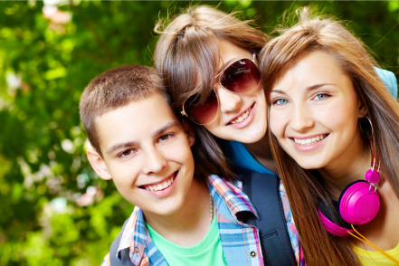 Three teens, a boy and two girls, one wearing sunglasses, smile at the camera.