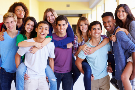 A group of teens gather in what looks like a school hallway. They appear to be supportive and like each other.