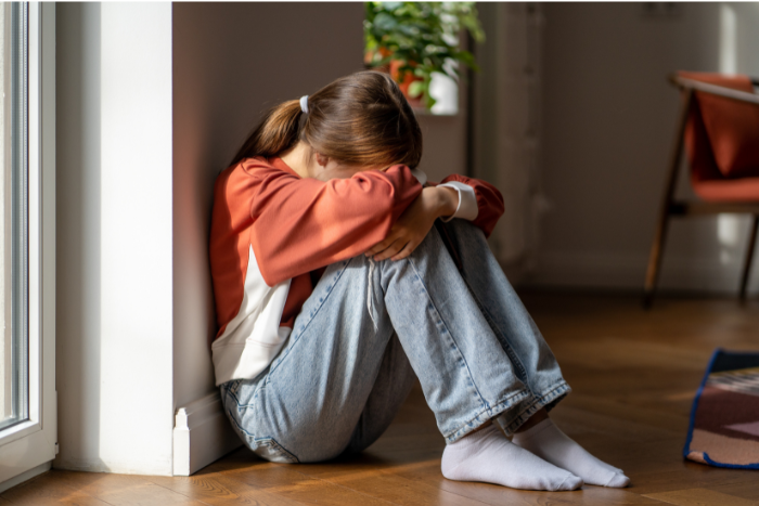 A teenage girl sits on the floor with her head on her knees, showing she is avoiding school.