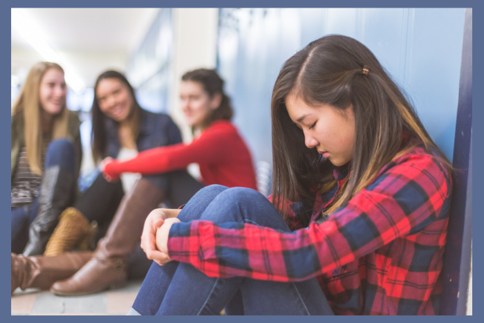 School avoidance can be a symptom of a mental health issue. In this photo a teen girl sits on the floor of a hallway at a school, looking sad.