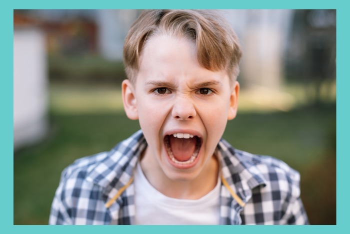 A young teenage boy screams. He's wearing a plaid shirt over a white t-shirt and looks very upset.