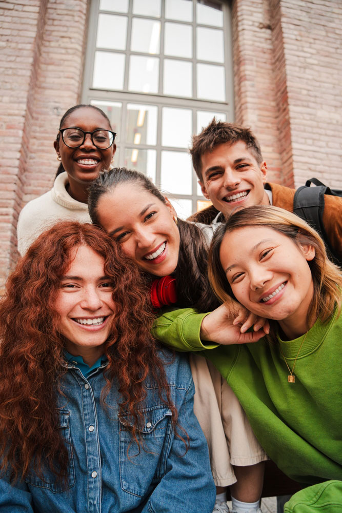 Group of teens standing outside a building huddled together and smiling