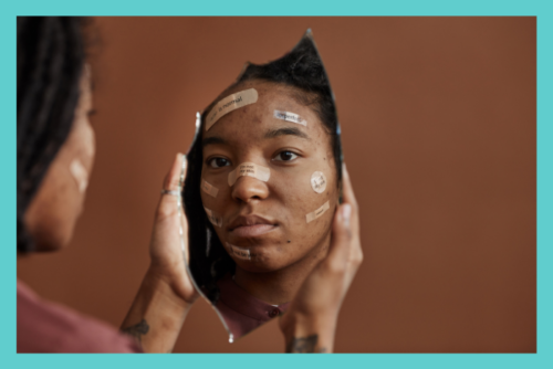 Person with facial bandages looks at their reflection in a broken mirror, conveying self-esteem and body-image challenges.